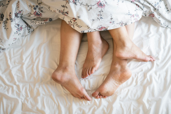 photo de quatre pieds nus emmêlés qui dépassent d'une couette, sur un lit